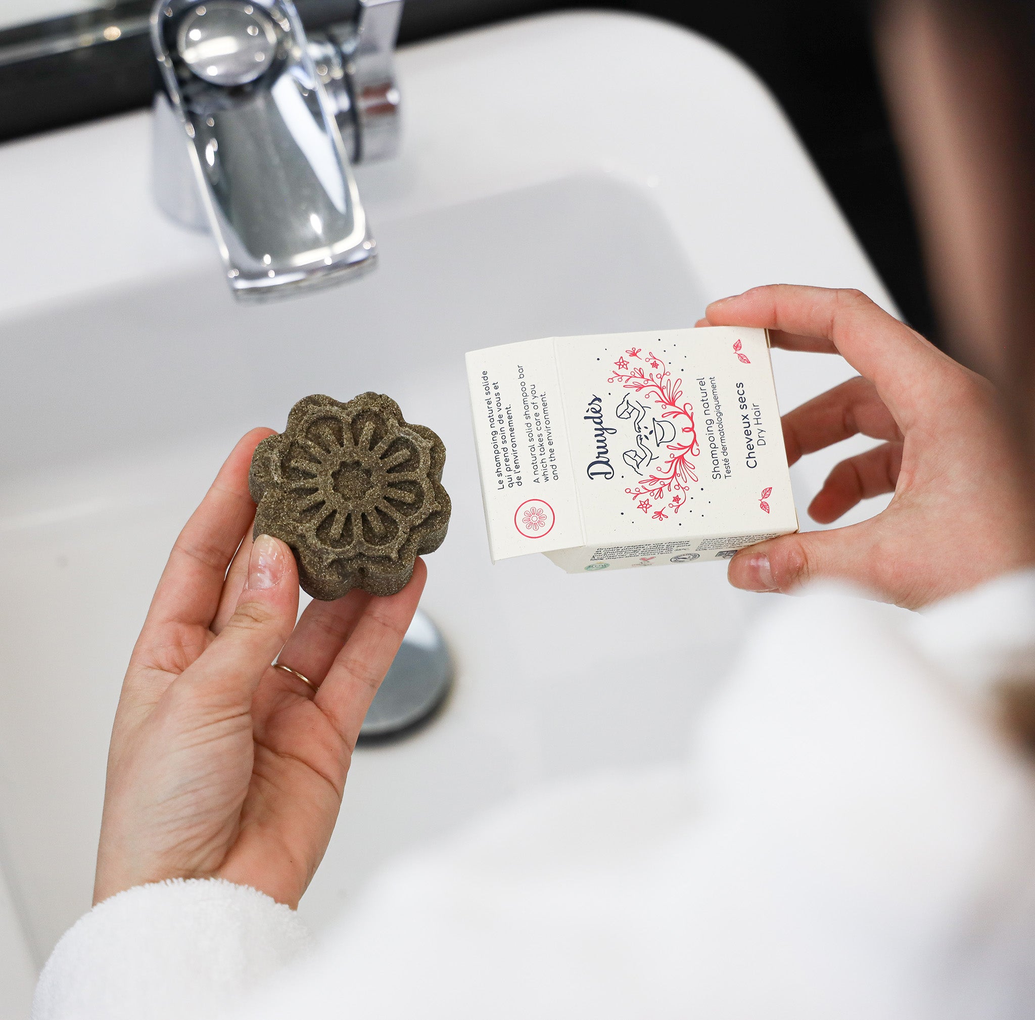 Shampoing solide de la marque druydès dans les mains d'une personne, au dessus d'un évier