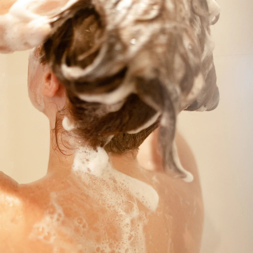 Vue de dos d'une personne féminine se lavant les cheveux avec l'après-shampoing Refyld
