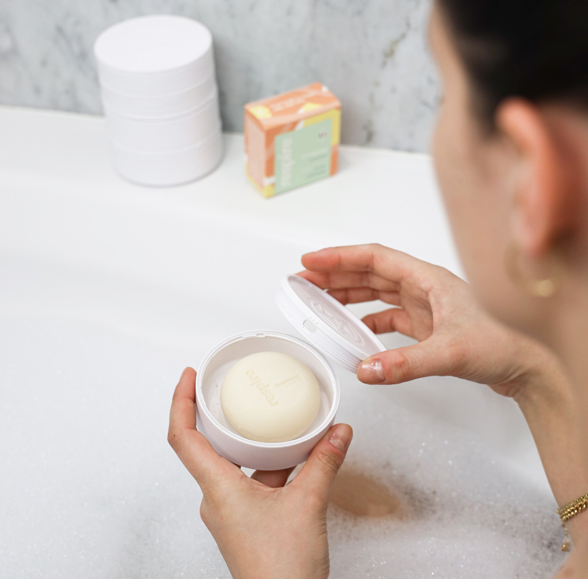 Shampoing rond solide de la marque respire au lait d'amande dans les mains d'une femme prenant son bain